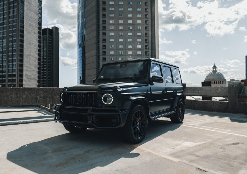 Black Mercedes G-Class SUV parked on a rooftop with city skyscrapers and a domed building in the background.